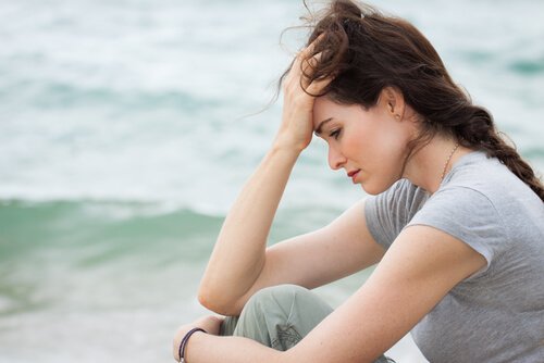 A worried woman sitting near the sea.