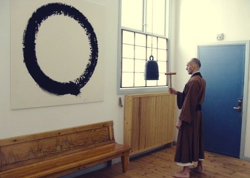 A Buddhist monk staring at an ensō circle on a wall.