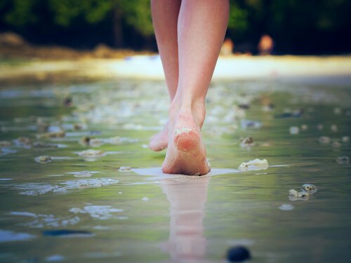 A photo showing a pair of feet walking along a road covered in a thin layer of water.
