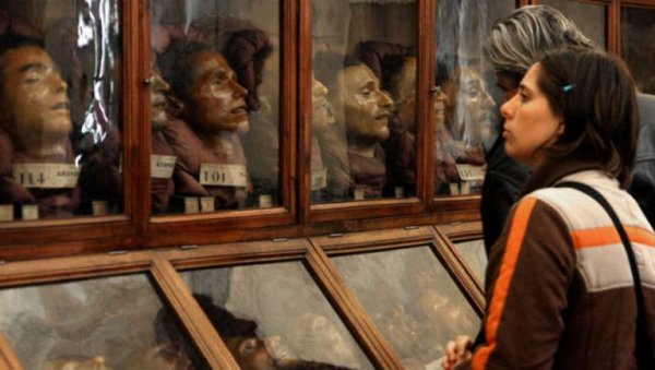 A couple standing in front of a series of glass display cases with replicas of human heads in them.