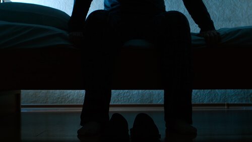 Man sitting on bed suffering from restless legs syndrome.