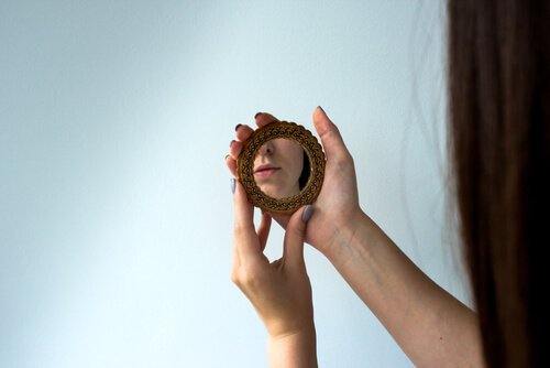 A woman looking at herself with a hand-mirror.