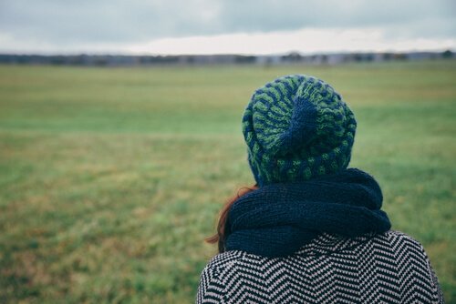 Woman feeling homesick and looking oout into a field thinking about her home.