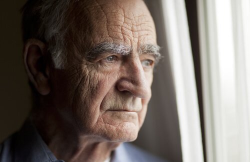 An old man looking out the window of a nursing home.