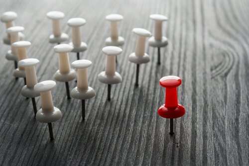 One red pushpin next to a triangle of white pushpins.
