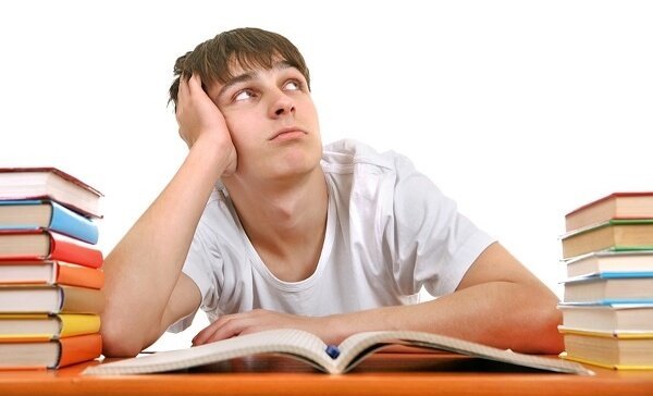 A bored teenager sitting at a desk with stacks of books, looking up at nothing, symbolizing the importance of educational neuroscience.