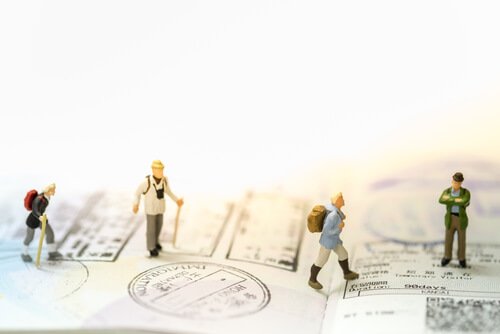 Tiny human figurines walking over a passport with backpacks and walking sticks.