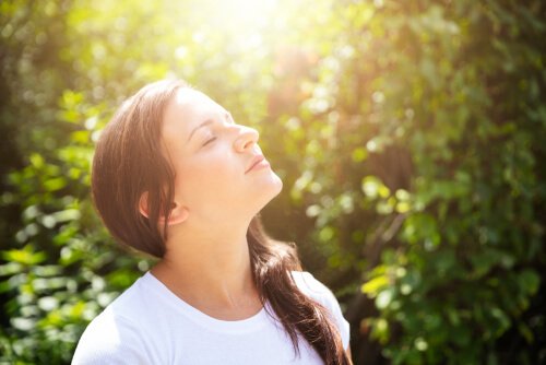 A picture showing a woman looking up with her eyes closed and taking in the nature around her.