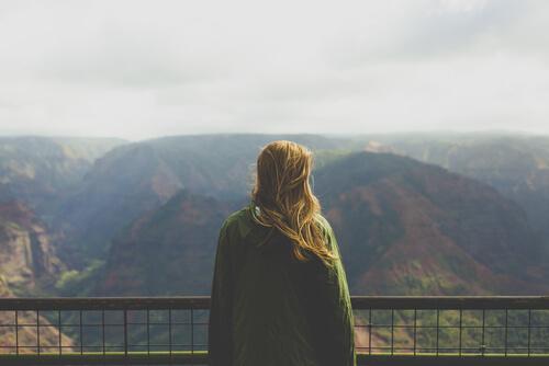 A woman standing at a mountain overlook and gazing out at the mountains in the distance.