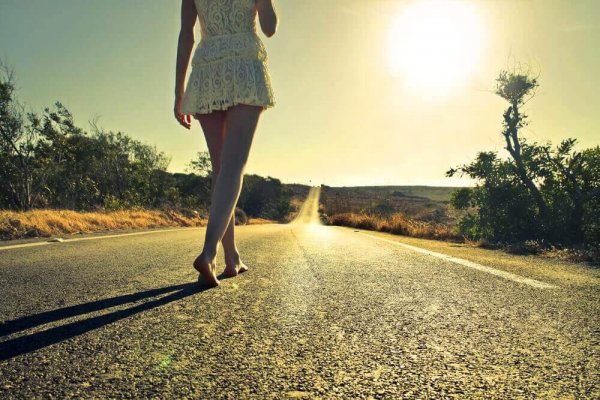 A woman walking barefoot in the middle of a country road.