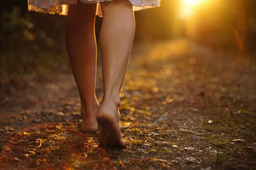 A woman walking barefoot on a path outside.