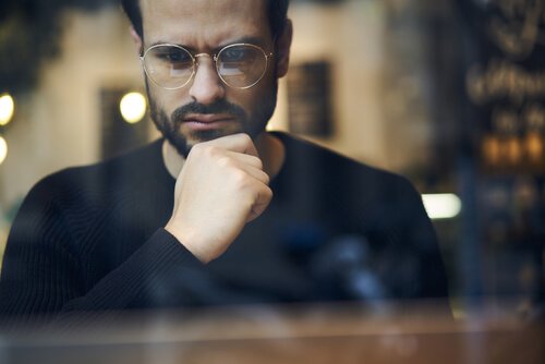 A guy with glasses thinking in a window.