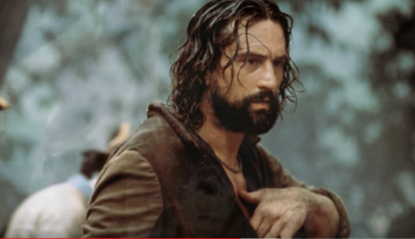 A still from The Mission showing Robert DeNiro holding his hand to his chest.