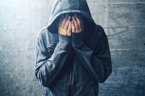 a man in a hoodie covering his face with his hands