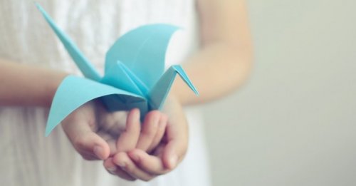A person holding a blue paper bird.