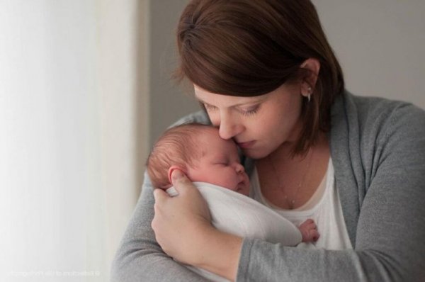 A mother is cradling her newborn baby in her arms, close to her neck.