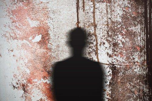 The outline of a person being cast as a shadow on a wall with dried blood on it.