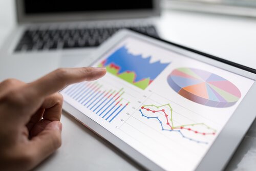 A person's hand hovering over a tablet screen displaying statistical charts and graphs.