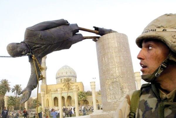 A picture showing a large group of people tearing down the statue of Saddam Hussein, while a US soldier looks on.