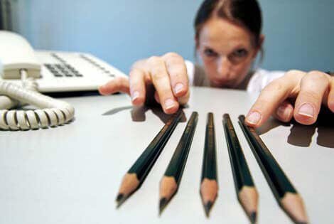 A woman sitting at her desk and meticulously ordering her pencils into a straight line.