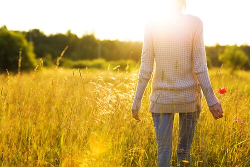 A person seen from the neck down walking through a sunny field, happy to live without fear.