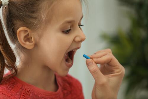 A child opening their mouth wide to take a pill.
