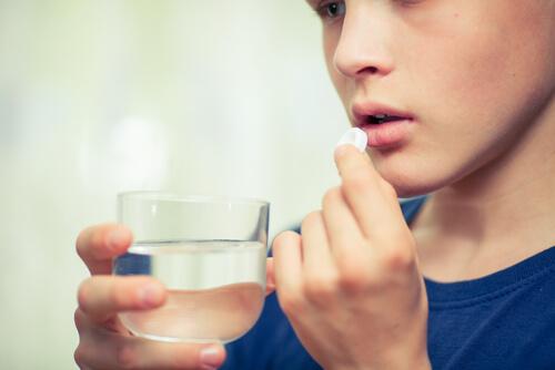A young person holding a cup of water as they prepare to take a pill, symbolizing the use of psychiatric drugs in children and teenagers.