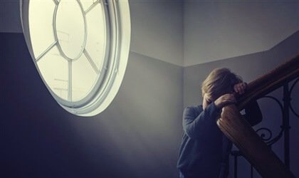 A little boy, seemingly scared, leaning on the staircase rail.