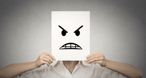 A person covering their face with a paper mask signaling they're angry.