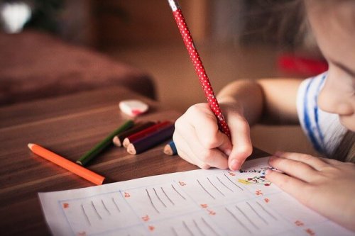 a little girl writing on paper with a pencil