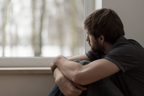 A man sitting by the window, looking outside and looking sad.