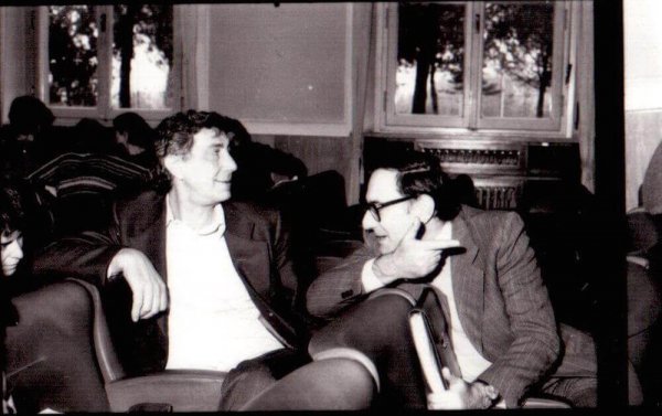 A photo showing Basaglia sitting in an armchair beside another man who's talking to him.