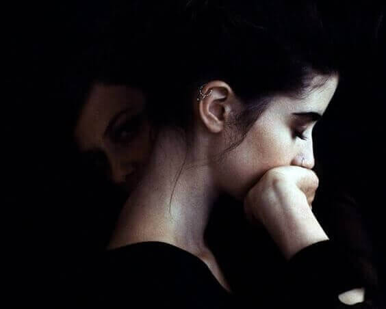 A woman in a dark space with a shadow of herself hiding in the background, covering her mouth.