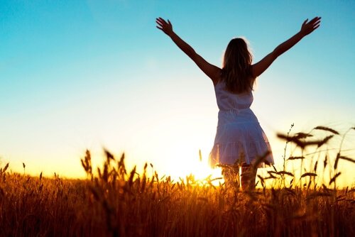 A happy woman standing in a field at sunrise, with her arms spread wide towards the horizon. 