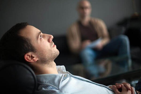 A man lying on a therapist's couch, practicing MR therapy for his sleep paralysis.