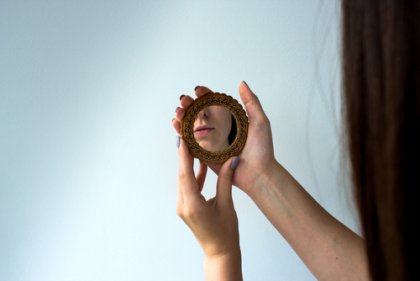 A woman looking into a hand mirror.