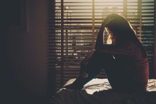 A woman sitting in a dark room with her hands on her head.