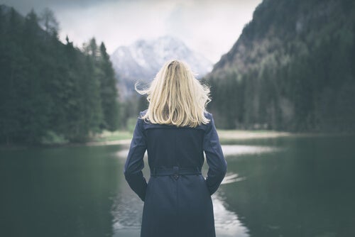 A blonde woman looking at the lake, from behind.