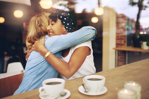 Two girlfriends hugging while having coffee.