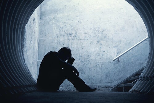 A man sitting down in a tunnel with his face in his hands. 