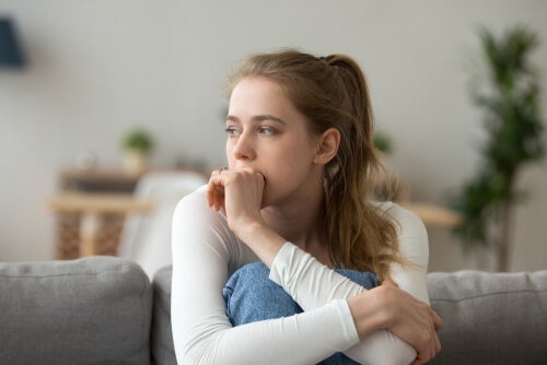 A woman sitting on the couch with her knees in her chest, looking thoughtful, or concerned. 