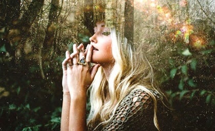 A woman sitting in the forest with her hands on her chin in thought.