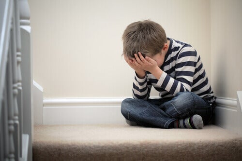 A boy sitting on the stairs in his home, crying.