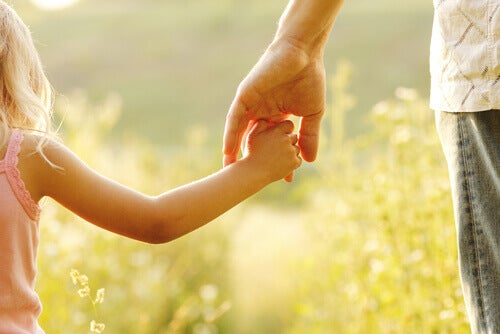 A child holding hands with their parent in a field. 