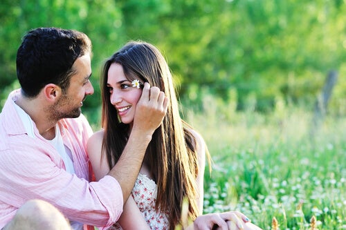 A couple sitting together in a field, looking into each other's eyes.