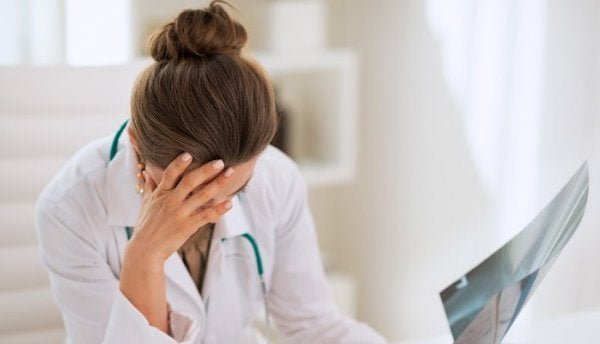 An exhausted doctor with occupational burnout syndrome holding her head in her hand.
