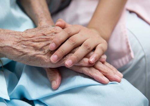 A young person putting their hand over an elderly person's in a hospital.