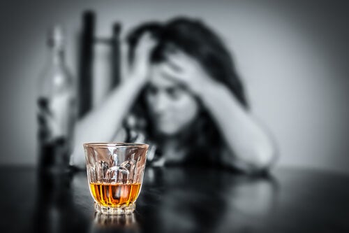 A woman sitting at a table with a shot of liquor a few feet away from her.