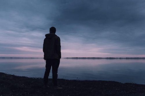 A sad man in front of a lake.