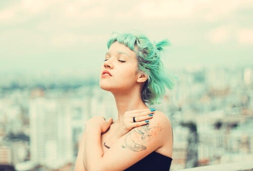 A woman with blue hair standing outside with her arms wrapped around herself.